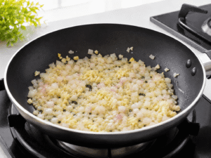 Diced onion, garlic, and ginger sautéing in hot olive oil inside a black frying pan with light steam rising.