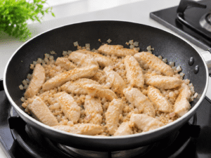 Chicken breast strips cooking with onions and garlic in a nonstick frying pan until lightly golden brown.