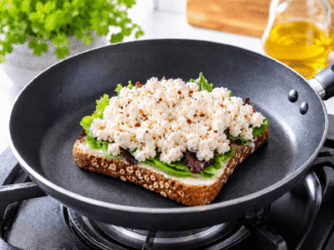 Bright food blog style cooking image showing seasoned cottage cheese mixture added on top of fresh salad greens over toasted whole grain bread in a frying pan.