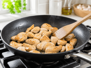 Chicken pieces cooking in olive oil in a black nonstick skillet until lightly golden and fully cooked.