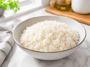 Warm cooked rice served in a white bowl ready to be topped with chicken and broccoli.