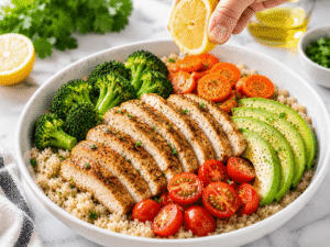 Fresh lemon juice being drizzled over a chicken quinoa bowl with vegetables and avocado