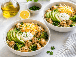 Keto chicken bowls topped with sliced avocado, shredded cheese, and sour cream for serving.