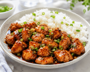 Spicy garlic chili chicken served hot with white rice on a ceramic plate in a bright kitchen setting.